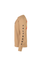 A tan long-sleeve performance shirt shown in a side profile view against a solid white background. The shirt features the word 'SALTBRED' printed vertically in black on the right sleeve and a red and yellow graphic on the left sleeve.