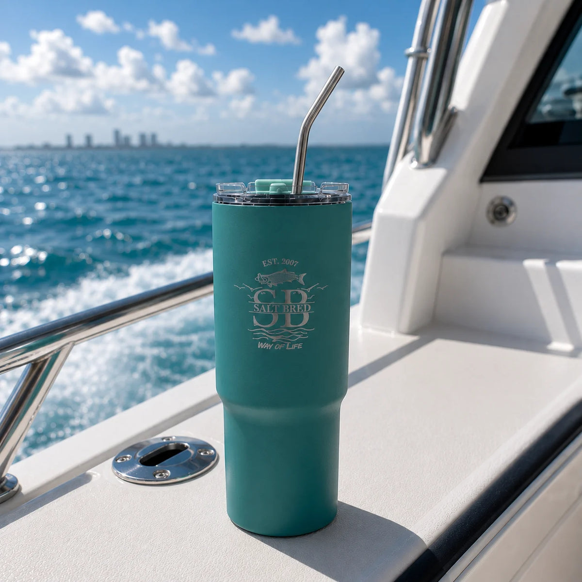 Teal tumbler with straw on a boat with ocean and city skyline in the background